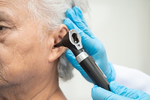 Otolaryngologist or ENT physician doctor examining senior patient ear with otoscope, hearing photo