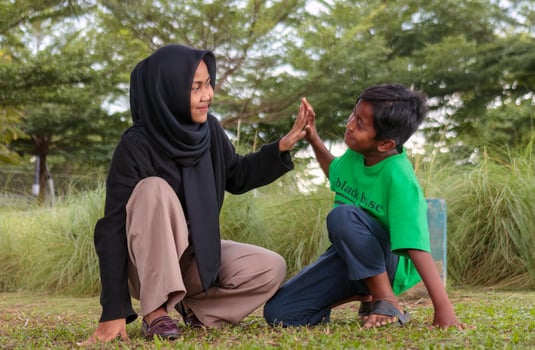 Muslim Woman and Boy High Fiving Outdoors in a Park photo