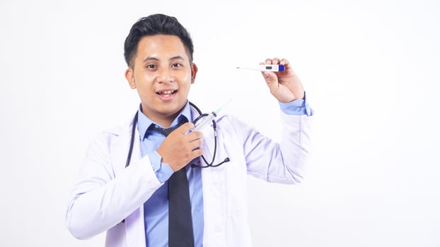 Smiling Asian Male Doctor Holding Syringe and Showing Thermometer on White Background photo