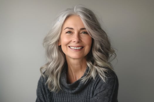 A smiling middle-aged woman with gray hair, wearing a cozy sweater, radiates warmth and confidence against a neutral background. photo