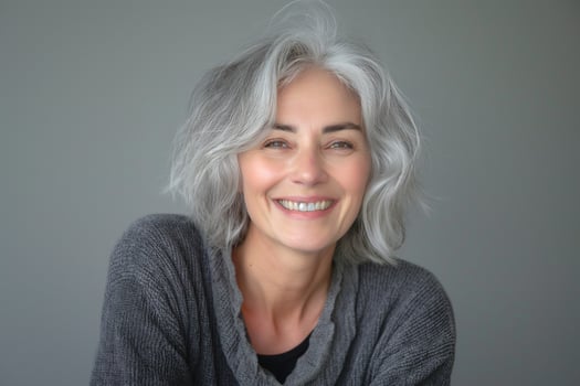 Smiling middle-aged woman with gray hair, wearing a cozy sweater, exuding warmth and confidence in a neutral background. photo