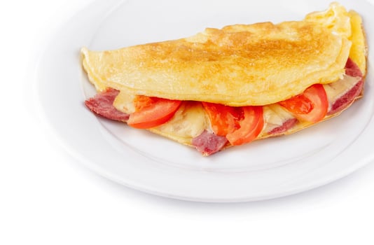 Folded omelette filled with cheese, ham and tomatoes on white plate close up photo