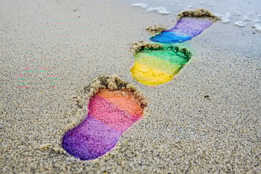 Rainbow colored footprints leading forward on sandy beach, symbolizing progress in rights activism during pride month photo