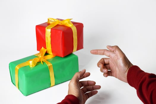 The hand of a person in a red sweater shows a red and green gift box photo