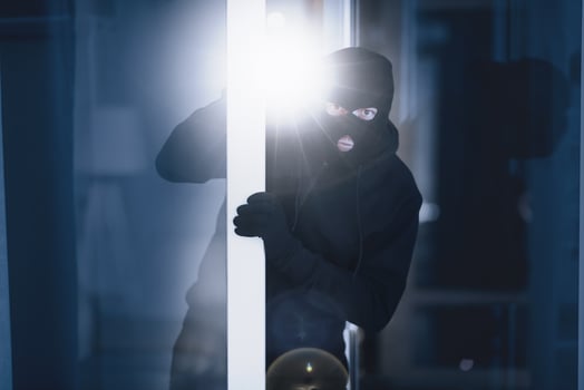 Burglary Concept. Evil intruder wearing black mask peeking into house through window or glass door, using flashlight photo