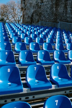 Rows of blue chairs are arranged in an amphitheater near an ancient stone building photo