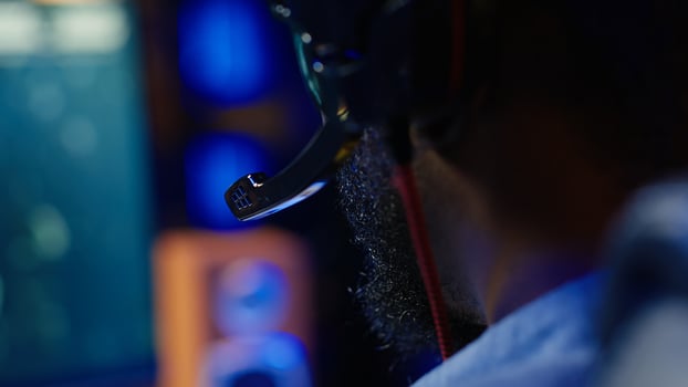 Man playing SF videogame on computer, having fun in neon lit apartment, close up. Gamer competing in online multiplayer game, using headphones to talk with teammates, camera A photo