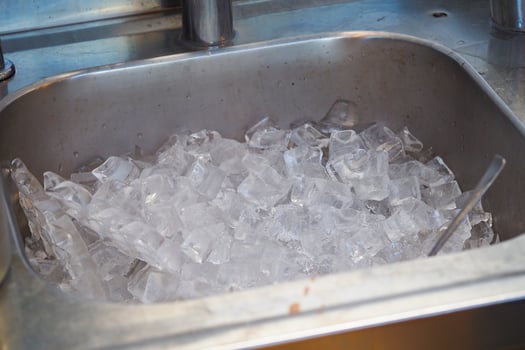 Ice cubes piled in a metal sink at a food preparation area photo