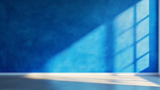 Sunlight streams through a window onto a blue wall, creating a bright, contrasting, geometric pattern. The room is simple, modern and empty. photo