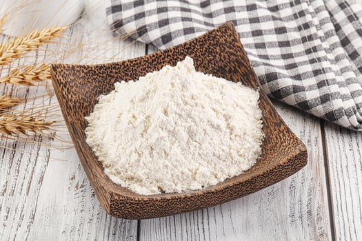 Wheat flour in a wooden bowl on a white wooden table photo