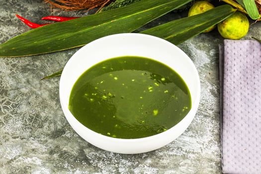 A bowl of green soup with a napkin on a table photo