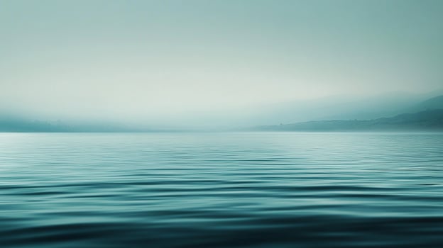 Serene turquoise landscape. Soft, misty mountains loom distantly over calm water rippling in the foreground. Quiet, peaceful, and scenic. photo
