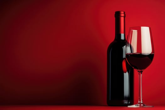 Elegant red wine in a glass beside a bottle on a red background photo