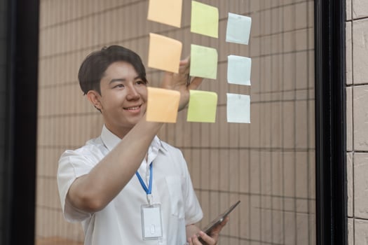 Young professional smiling while arranging sticky notes on glass wall, organizing tasks and improving workflow in modern office. photo