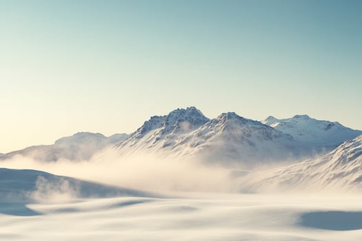 Serene snowy mountain range, the peaks covered in a blanket of white against the pale blue sky, a peaceful and majestic winter landscape. photo