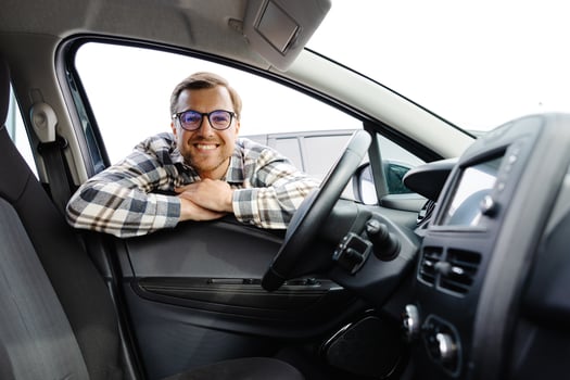 Man looking through window inside new car, checking it before purchase at modern dealership store. Cheerful guy buying or renting automobile at showroom. photo
