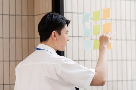 Young businessman organizing colorful sticky notes on glass wall for project planning in modern office. photo