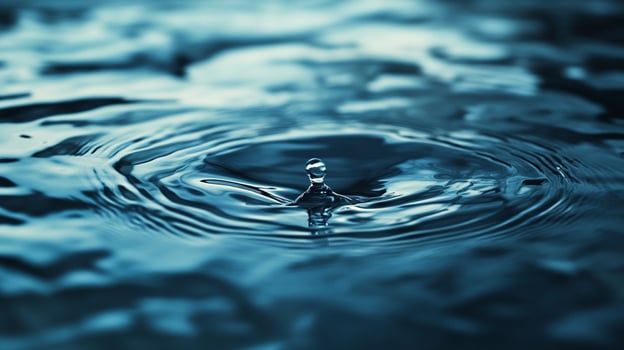 A solitary drop of water gracefully falls into a tranquil surface, creating ripples that symbolize serenity and depth in a calming visual display. photo