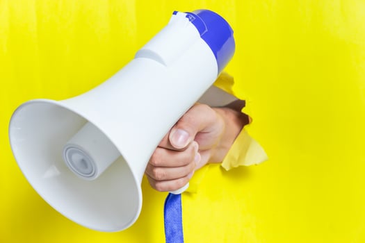 A hand holding a megaphone through a yellow wall, demonstrating loud communication photo