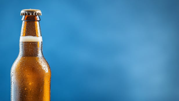 A chilled bottle of beer with condensation against a blue background. photo