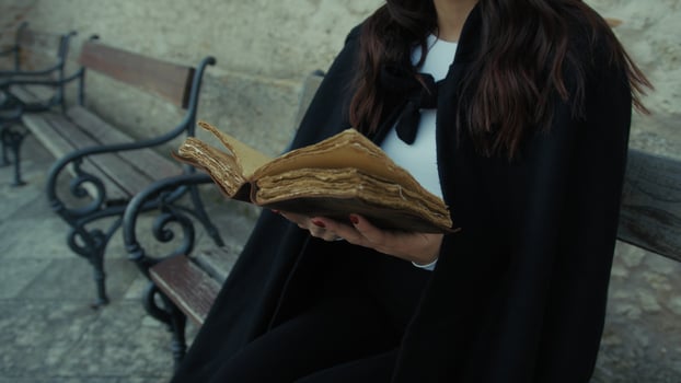 Woman With Cloak Reads The Mysteries In The Book Sitting On A Bench In The City photo