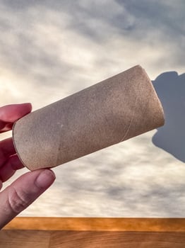 Hand holding an empty cardboard toilet paper roll with soft shadow on wall. High quality photo