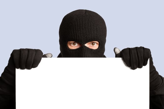 Masked gangster holding and looking out white blank board, isolated over white studio wall photo