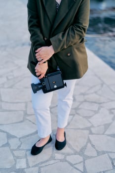 Old film camera is in the hands of a young woman standing on the tile. Cropped photo