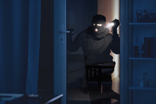 Vandalism Concept. Disguised villain with torch watching enclosed property through balcony glass door photo