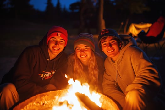 Smiling siblings enjoying a warm campfire outdoors on a cool evening under the night sky photo