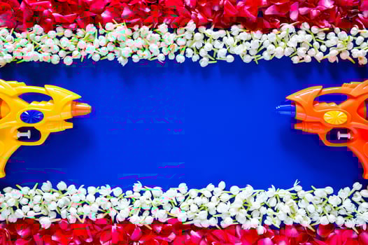 Water guns with jasmine and red rose petals on empty blue background which set as Thailand flag for Thailand songkran festival concept. photo