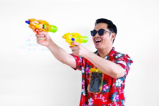 Thai male having fun with blurred focus of water gun shooting and wearing colorful shirt with waterproof case for Thailand Songkran festival concept. photo