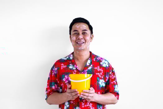 Thai male with white clay filler on face wearing colorful shirt holding bucket for Songkran or Water festival in Thailand concept. photo