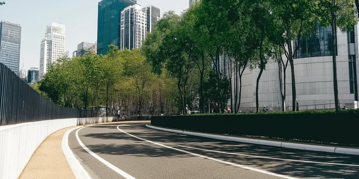 Empty asphalt road winding through a modern city with green trees and skyscrapers nearby photo