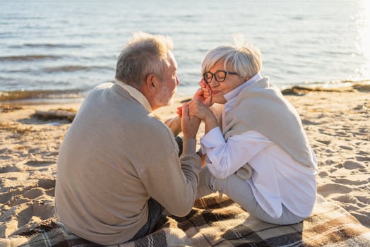 Senior mature couple sitting on beach holding hands enjoying outdoor recreation. Old husband wife touching hands with tenderness love. Grandmother grandfather together. Family moment of love photo