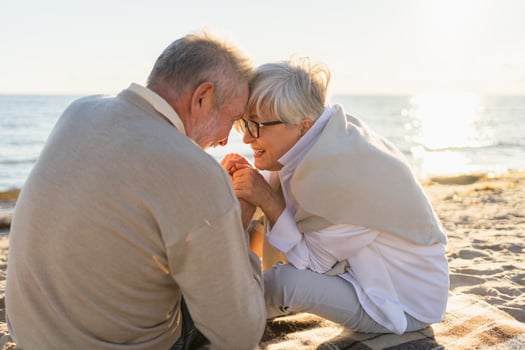 Senior mature couple sitting on beach holding hands enjoying outdoor recreation. Old husband wife touching hands with tenderness love. Grandmother grandfather together. Family moment of love photo