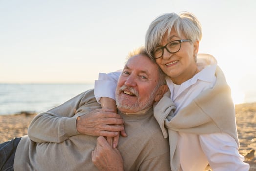 Senior mature couple sitting on beach hugging enjoying outdoor recreation. Old husband wife embracing with tenderness love enjoying sweet bonding. Grandmother grandfather together. Family moment love photo