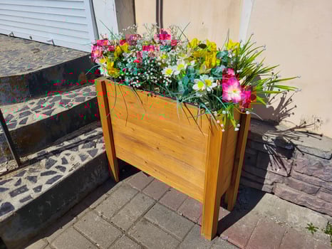 Artificial multicolored flowers in a wooden flowerbed on legs near the porch. photo