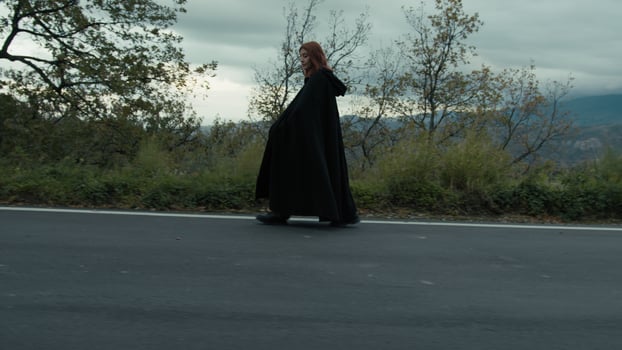 Enigmatic Secure Woman Walks With A Long Black Cloak In The Mountain Road photo