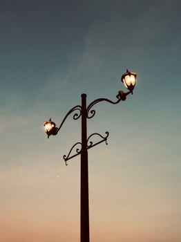 A vintage street lamp from a low angle warm light contrasts a sky shifting from dusk blue to soft orange. Twilight's nostalgic charm crowns this serene sentinel. photo