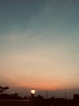 A cozy cafe corner with a vintage lamp casting soft glow as twilight paints the sky in warm orange, pale blue. Distant towers silhouette against dusky sky, adding a tranquil depth. photo