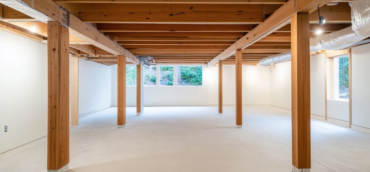 Empty basement with wood beams, windows, and white walls photo