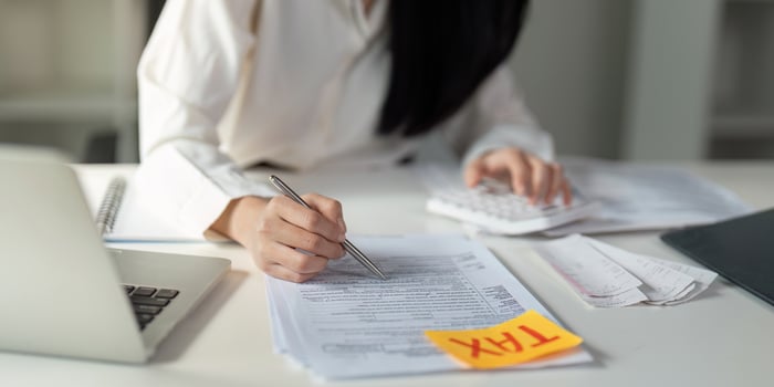 Close-up of a young woman writing on tax documents while using a calculator in her office. photo