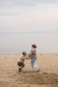 Hand in hand, a brother and sister in plaid jackets stroll along the coastline, leaving footprints in the sand. photo