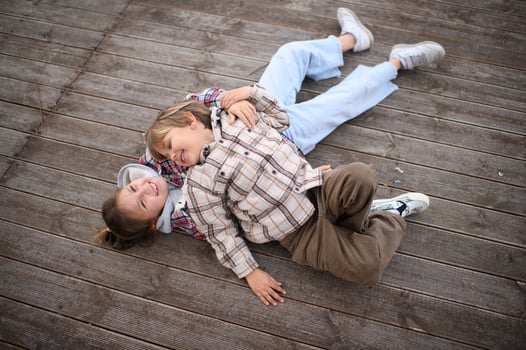 Dressed in plaid shirts, two children lie on a wooden deck by the ocean, playing and sharing a moment of happiness. photo