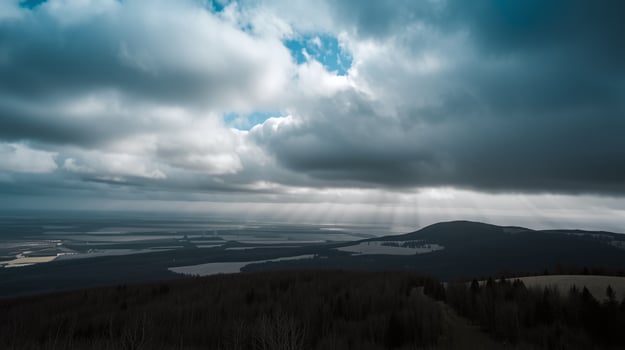 Amidst dense clouds, sunlight pierces through, illuminating vast, tranquil landscapes below. photo