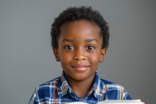 A smiling Black boy with curly hair holds a book, conveying curiosity and joy in a neutral-toned setting. photo