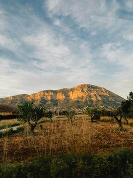 Mountain during golden hour. Majestic Puig Campana mountain basking in warm glow of setting sun, seen from cultivated field with olive trees in foreground, creating picturesque scene in Alicante Spain photo