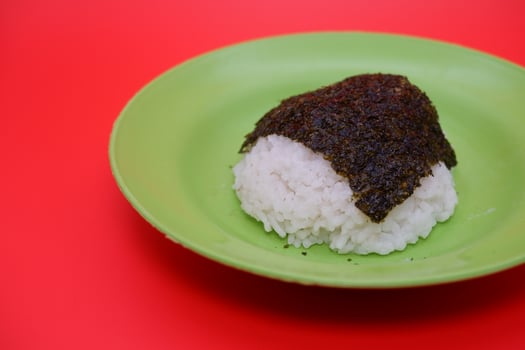 Rice Topped with Dried Nori Seaweed on a Green Plate, Isolated on Red Background photo