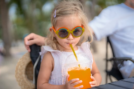 Young girl enjoying a colorful drink while sitting outdoors at a sunny beachside location photo